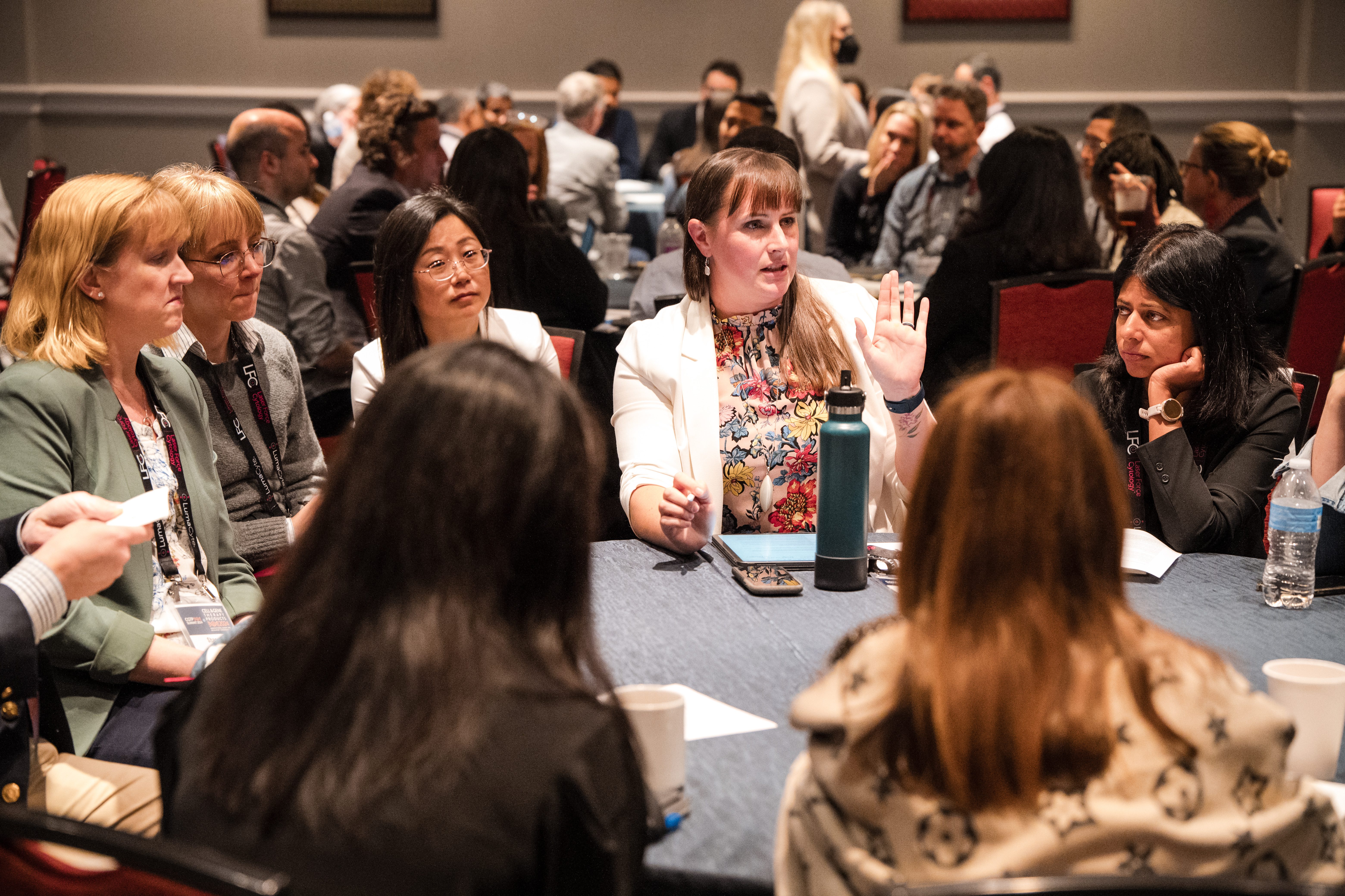 Group around a table discussing topics.  Woman raising hand to discuss.