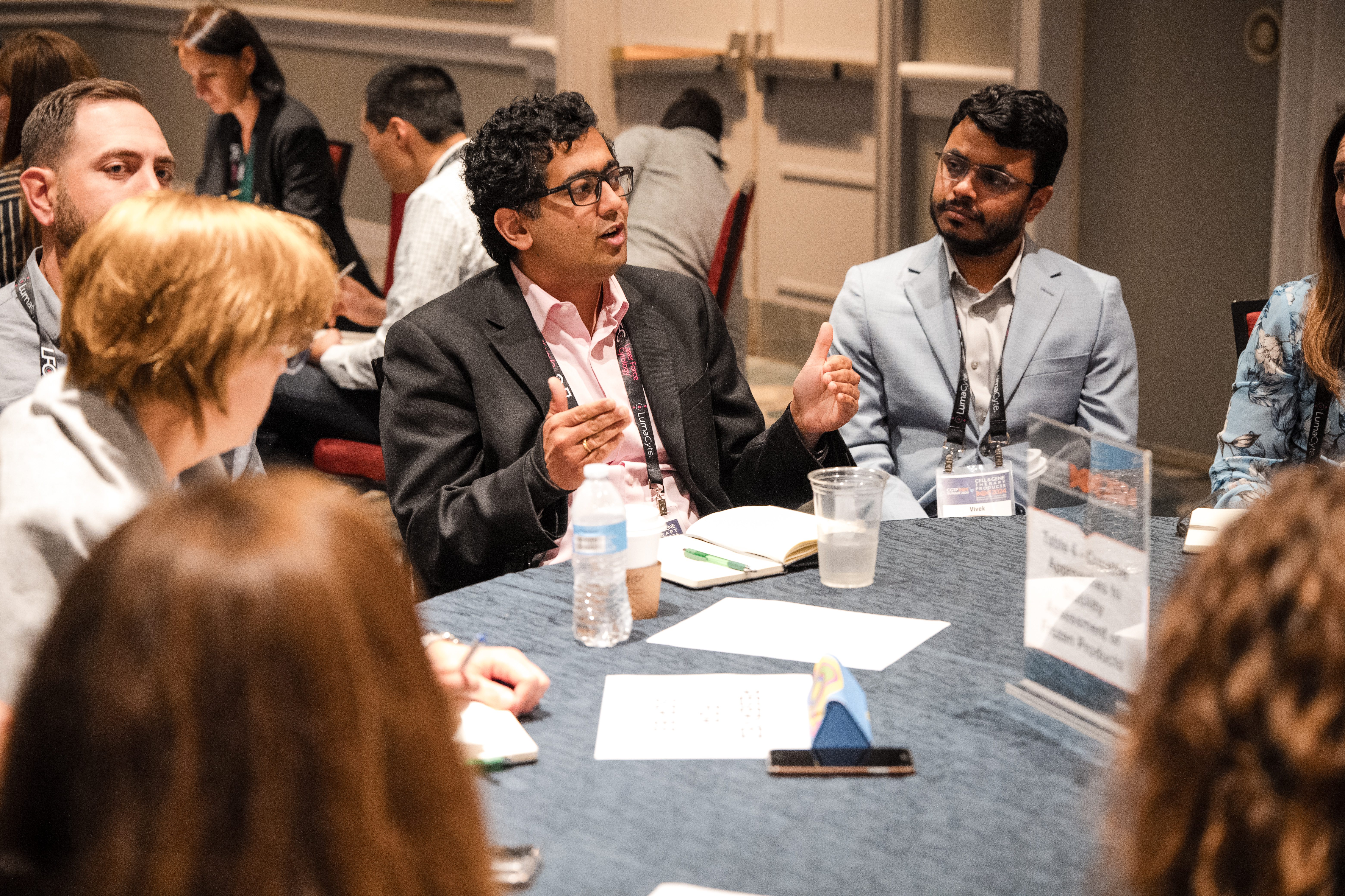 People around table discussing topics. Focus on man with hand motions while discussing.